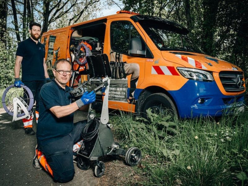 Das Team von Dihn Kanalreinigung hilft bei Rückstau. Die Mitarbeiter posieren vor ihrem orangefarbenen Einsatzfahrzeug.